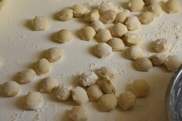 Around twenty homemade dumplings arranged on a white surface with flour, traditional food preparation.