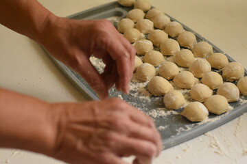 Homemade dumplings neatly arranged on a gray plastic cutting board, visible hands preparing traditional food.