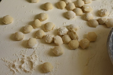Scattered raw dumplings on a white table with flour, homemade traditional food preparation.
