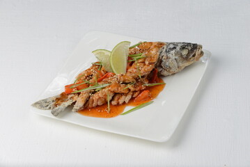 fried fish with head in sauce in a white plate on a white background 