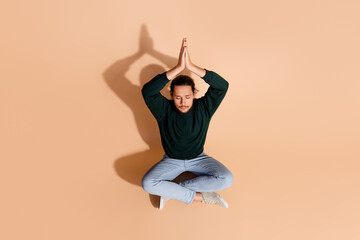 Young man meditating in a seated pose with hands together against a beige background showcasing tranquility and balance