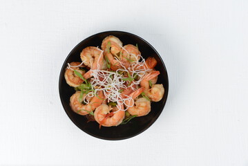 Shrimp in a black plate with chili pepper on a white background