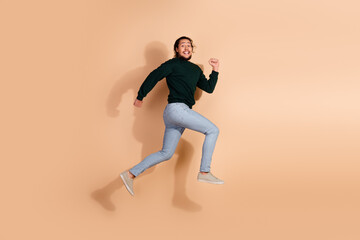Energetic young man in casual clothes enthusiastically jumping against a beige background showcasing fun and dynamic vibe