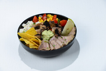 bowl of veal tacos in a black plate with chili peppers and herbs on a white background