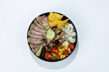 bowl of veal tacos in a black plate with chili peppers and herbs on the background