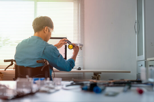 Asian engineer in wheelchair building robot in modern office - Powered by Adobe