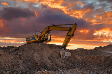 Obraz premium Excavator on earthmoving on sunset. Digger on construction site. Excavator moving soil. Heavy Machinery in open-pit mining. Earthmover on earthmoving in sandpit. Groundworks construction site.