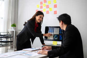 Businesswoman pointing at charts on computer screen during meeting with businessman