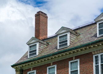 Historic brick building with dormer windows and slate roof under cloudy sky in Cambridge, Massachusetts, USA