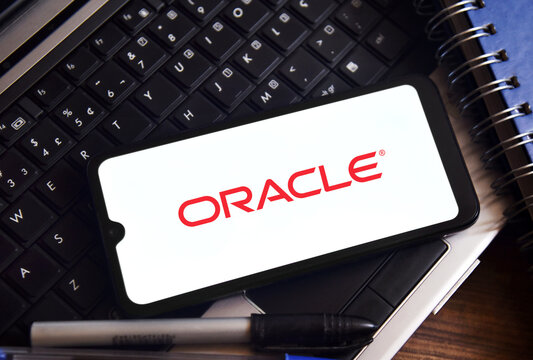 Oracle logo on a smartphone screen with a laptop and accessories in the background. Technology and business concept.