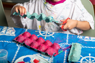 Child painting an egg box with a brush