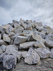 Low angle view of a pile of rocks against cloudy sky. These stones may be used for a variety of purposes, such as construction, road paving, or landscaping.