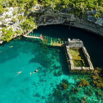Turquoise cenote with swimmers and wooden platforms
