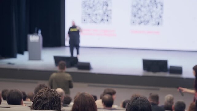 Focused view on audience with presenter on stage giving lecture during formal conference session. - Powered by Adobe