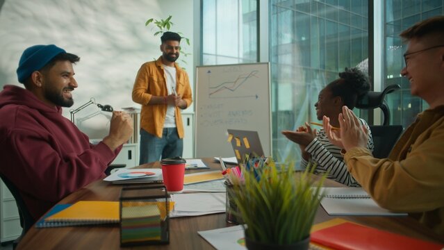 Successful startup presentation in casual coworking office diverse multicultural informal business team applauding male leader showing growth chart on whiteboard celebrating achievement work progress