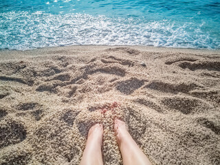 A peaceful beach scene with feet buried in soft sand near the shore of the Mediterranean Sea in Alanya, Turkey. The gentle waves and sparkling water create a relaxing atmosphere