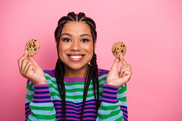 Naklejka premium Cheerful young woman in a colorful outfit holds chocolate chip cookies against a pink background with a bright smile