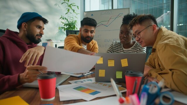 Focused concentrated informal casual startup business team considering paper document report information together talking solving finance problem multiethnic four people in office meeting with laptop - Powered by Adobe
