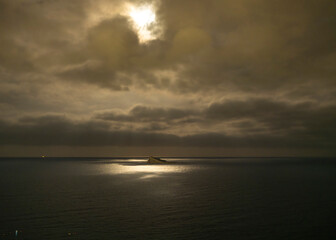 A mysterious lunar landscape over an island near Benidorm, Spain, with dramatic clouds casting shadows across the calm sea. The glowing reflection creates a surreal, cinematic atmosphere.