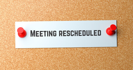 Meeting rescheduled text on white paper note pinned to cork board with red push pins, business schedule change reminder concept.