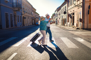 Happy senior tourist with suitcase walkig through the city on pedestrians crosswalk.