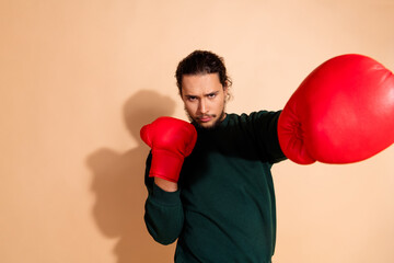 Portrait of a determined young man in red boxing gloves, with a casual green pullover against a beige background