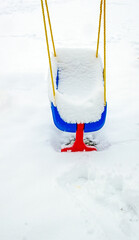 White fluffy snow fills a blue and red baby swing. The yellow ropes add more eye catching color to the winter scene.