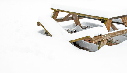 Snow covered wooden picnic table suffers a broken bench. A handyman with carpentry skills will be needed.