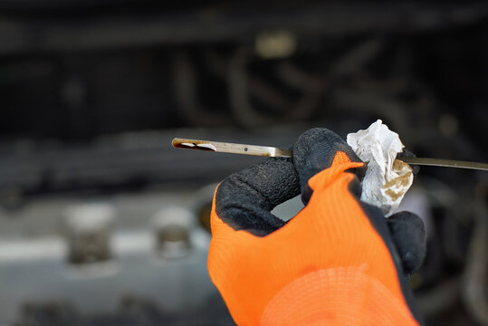 Oil dipstick tool used by auto mechanic to check engine oil level during routine maintenance, lubrication level inspection and car service. Close up view of engine oil dipstick, fluid level control