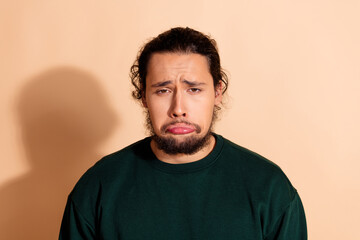 Fototapeta premium Young man in a green sweatshirt displaying a humorous sad pouty expression against a warm beige background