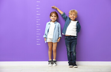 Obraz premium Cute little girl and boy measuring their heights near violet wall with scale