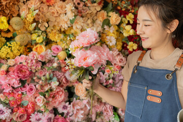 Asian female florist in apron smiling while designing a beautiful floral arrangement with her colleague in a flower shop. Concept of teamwork, creativity, floral business, and joyful workplace.