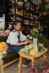 Asian female florist in apron smiling while designing a beautiful floral arrangement with her colleague in a flower shop. Concept of teamwork, creativity, floral business, and joyful workplace.