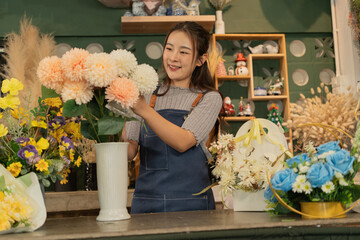 Asian female florist in apron smiling while designing a beautiful floral arrangement with her colleague in a flower shop. Concept of teamwork, creativity, floral business, and joyful workplace.