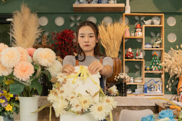 Asian female florist in apron smiling while designing a beautiful floral arrangement with her colleague in a flower shop. Concept of teamwork, creativity, floral business, and joyful workplace.