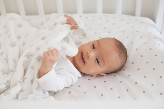 Smiling baby on white bedding with soft fleece blanket