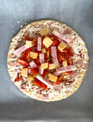 Homemade pizza with ham, tomatoes and cheese before baking