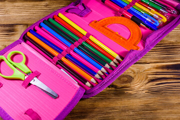 Different school stationeries (pens, pencils, ruler, protractor and scissors) in a pink pencil box