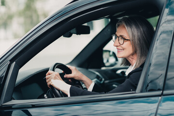 Confident senior woman driving a car in urban city environment, showcasing professional elegance and experience on a sunny day