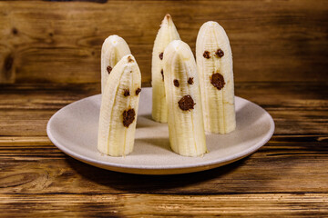 Scary banana ghosts in ceramic plate on a wooden table. Halloween concept