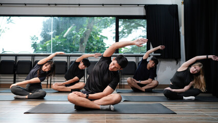 Diverse sporty men and women doing stretching exercises during group yoga lesson