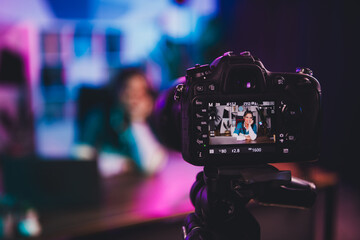 Young female vlogger recording a professional podcast in a cozy home studio with neon lights in the evening