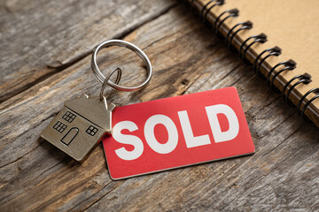 Home sale keychain and sold sign on rustic wooden table showing successful real estate transaction