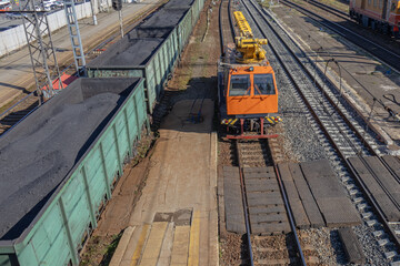 A crane on a small railway locomotive for the repair of railway tracks. Repair equipment on the railway.  Freight wagons filled with coal. Transportation of industrial raw materials by rail.