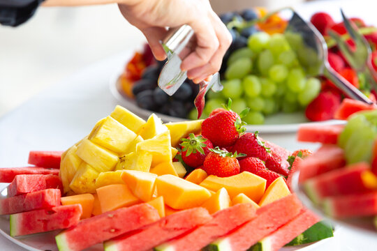 Caterer serving strawberries on fresh fruit platter at buffet table