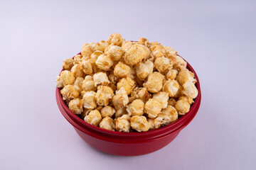 Close up of caramel popcorn in a red bowl, crunchy sweet snack with golden coating, isolated on light background