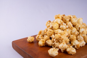 Pile of caramel popcorn on wooden cutting board, crunchy golden sweet snack isolated on light background, perfect for food photography and snack concept