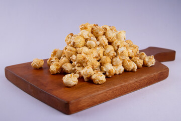 Pile of caramel popcorn on wooden cutting board, crunchy golden sweet snack isolated on light background, perfect for food photography and snack concept