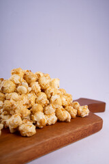 Pile of caramel popcorn on wooden cutting board, crunchy golden sweet snack isolated on light background, perfect for food photography and snack concept