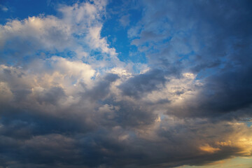 Dark approaching clouds reflect the bright light of the setting sun in the blue sky close-up.